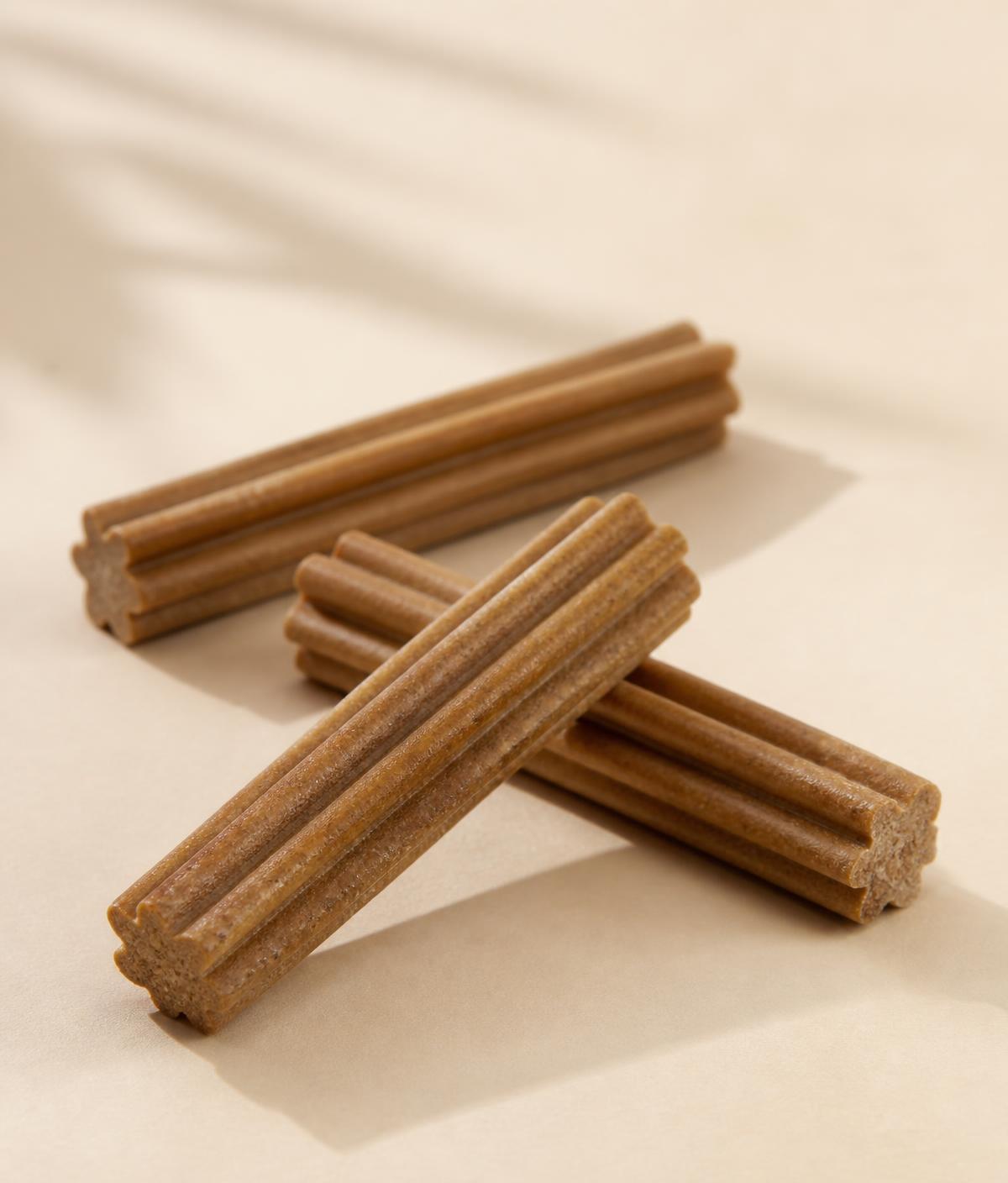 Three ridged Happiest Wags dental sticks on a warm neutral background